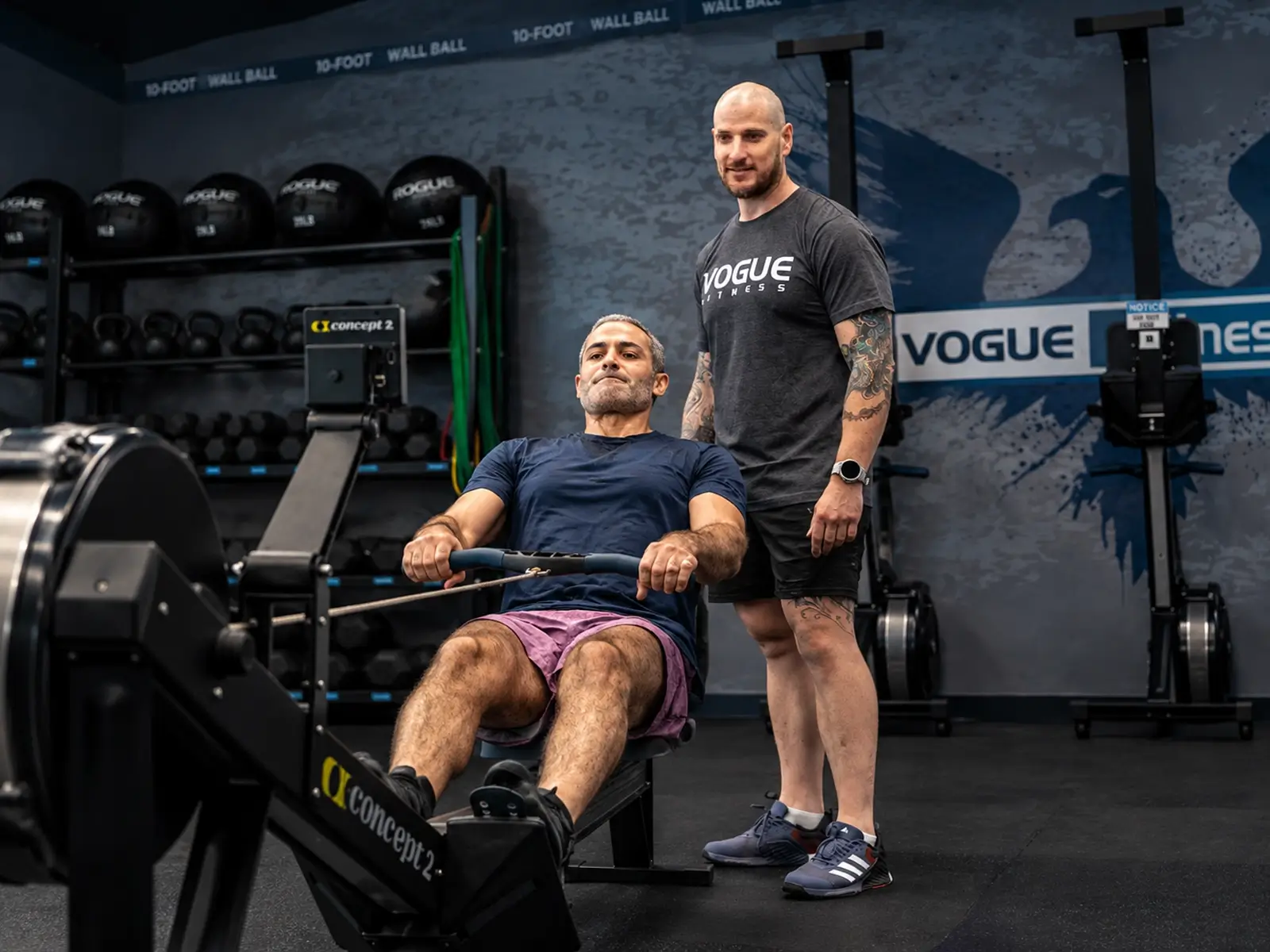 Vogue Fitness personal trainer supervising a member on a rowing machine